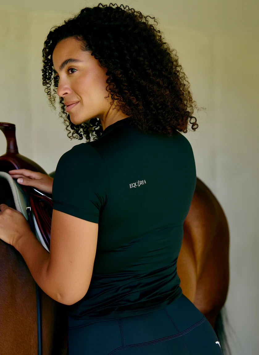 Amazzone con la maglia Equiria scura mentre sella il cavallo