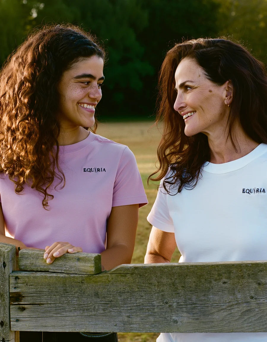 Due amazzoni sorridenti con le maglie Equiria rosa e bianca, appoggiate a uno steccato